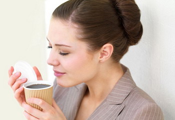 Side view of a young business woman smelling coffee